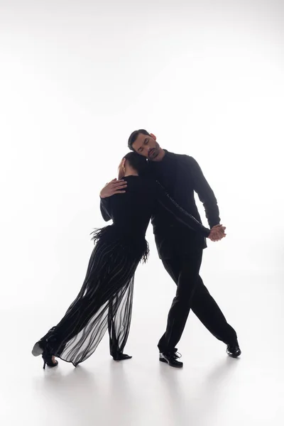 Bailarina de salão abraçando parceiro no vestido enquanto dança tango no fundo branco — Fotografia de Stock