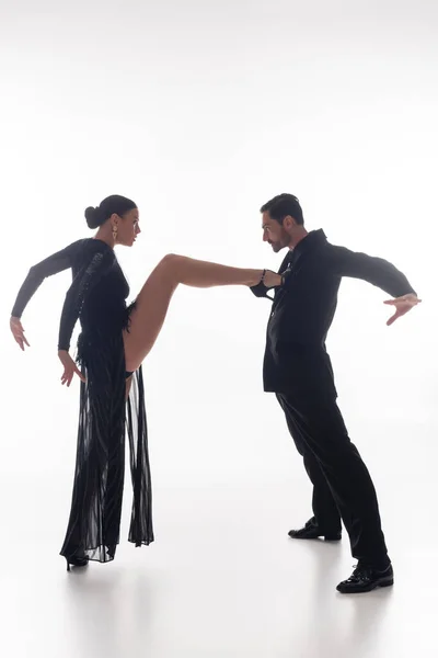 Vista lateral de mujer elegante realizando tango con pareja sobre fondo blanco - foto de stock