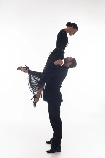 Side view of professional ballroom dancer lifting partner on white background — Stock Photo