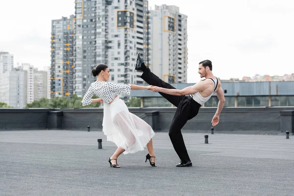Вид збоку веселих професійних танцюристів, що рухаються на даху будівлі — стокове фото