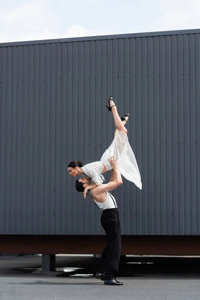Вид сбоку улыбающейся танцовщицы, поднимающей партнера на каблуках на крыше здания — стоковое фото