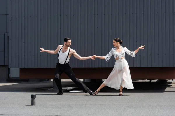 Bailarines de salón alegres tomados de la mano en el techo de la construcción al aire libre - foto de stock