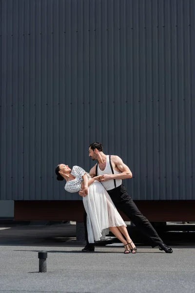 Vue latérale des danseurs professionnels se déplaçant et tenant les mains du toit du bâtiment à l'extérieur — Photo de stock