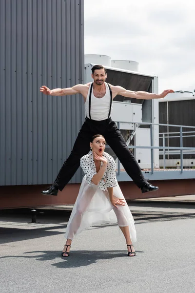 Danseuse souriante sautant près d'un partenaire choqué sur le toit du bâtiment à l'extérieur — Photo de stock