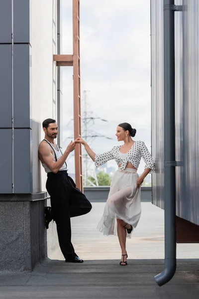 Smiling professional dancer touching hand of partner on rooftop of building outdoors — Stock Photo