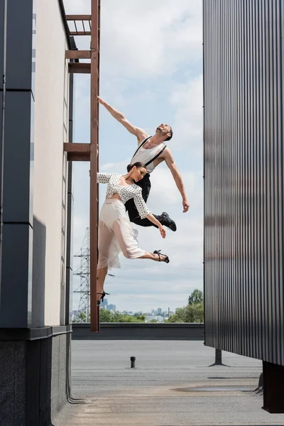 Cheerful professional dancers posing on ladder on roof of building outdoors — Stock Photo