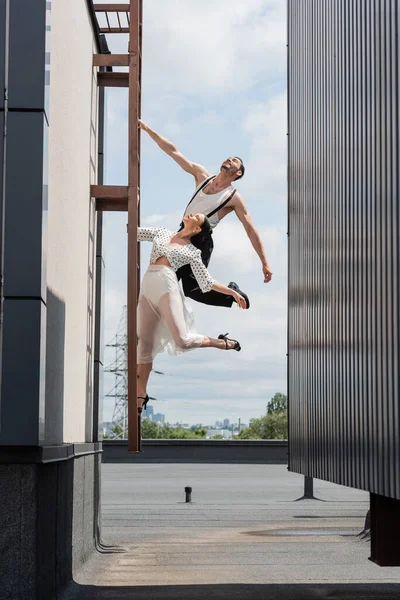 Positive Tänzer posieren tagsüber auf Leiter auf Hausdach — Stockfoto