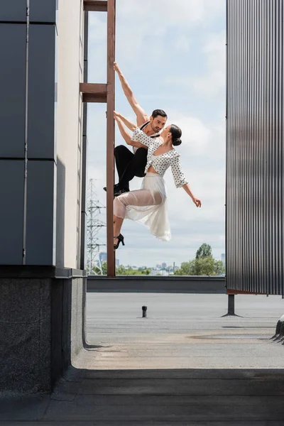 Professional ballroom dancers looking at each other while posing on ladder on rooftop of building outdoors — Stock Photo