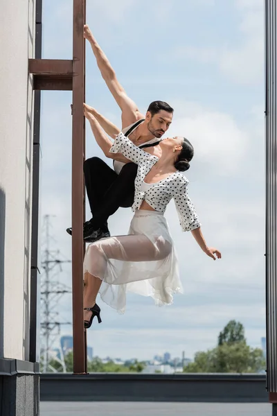 Danseurs professionnels embrassant tout en posant sur l'échelle sur le toit du bâtiment pendant la journée — Photo de stock