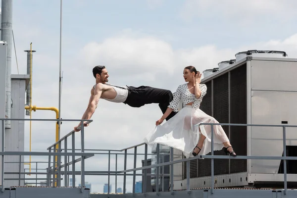 Stylish professional dancer looking at smiling partner on railing on building roof — Stock Photo