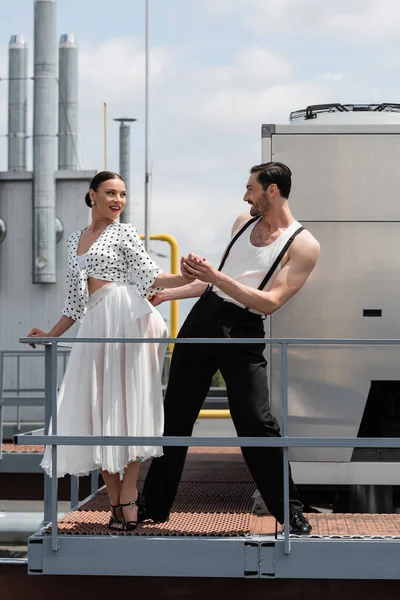 Bailarines alegres tomados de la mano mientras se mueven cerca de barandilla en el techo del edificio al aire libre - foto de stock