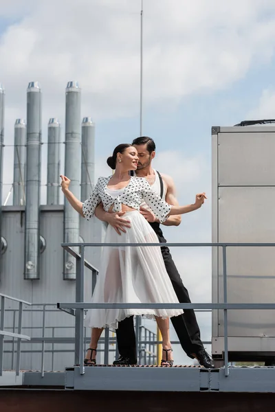 Elegante bailarina abrazando a su pareja sonriente mientras baila en el techo del edificio al aire libre - foto de stock