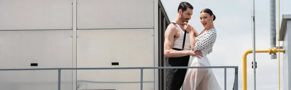 Cheerful and stylish professional dancer touching suspenders on partner on roof, banner — Stock Photo