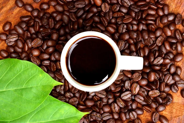 Geröstete Kaffeebohnen auf Holz und schwarzem Kaffee. — Stockfoto