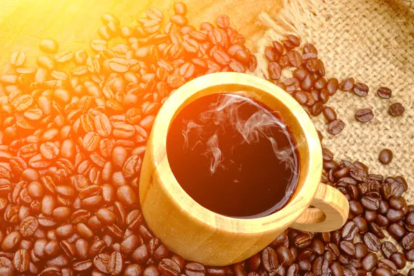 Pražená kávová zrna na dřevě a ranní černá káva ve skle — Stock fotografie