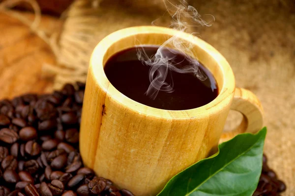 Pražená kávová zrna na dřevo a černá káva v dřevo sklo. — Stock fotografie