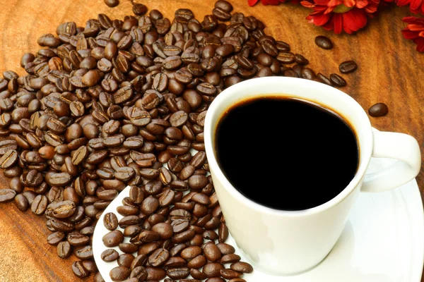 Xícara de café e grãos em um fundo de madeira . — Fotografia de Stock