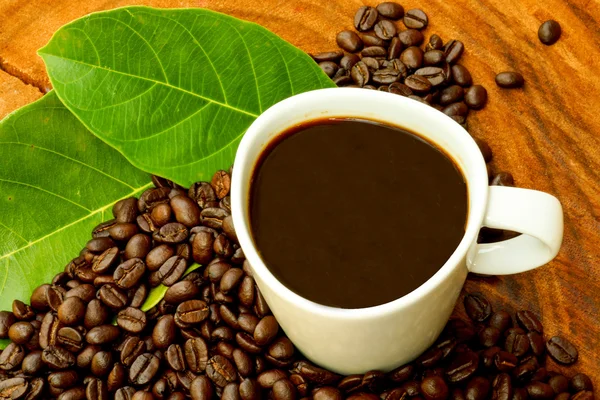 Xícara de café e grãos em um fundo de madeira . — Fotografia de Stock