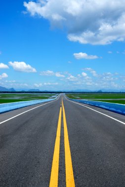 Empty road and the yellow traffic lines with blue sky. clipart