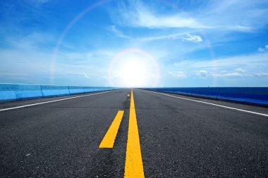 Empty road and the yellow traffic lines with blue sky. clipart