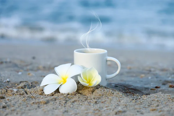 Koffie op het strand en frangipani bloem. — Stockfoto
