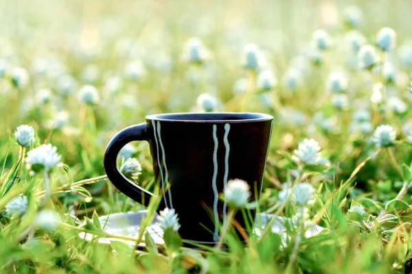 Café de la mañana con taza negra en el fondo de hierba de la flor . —  Fotos de Stock