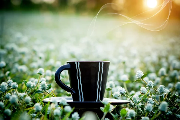 Café du matin avec tasse noire dans le fond de l'herbe de fleur . — Photo