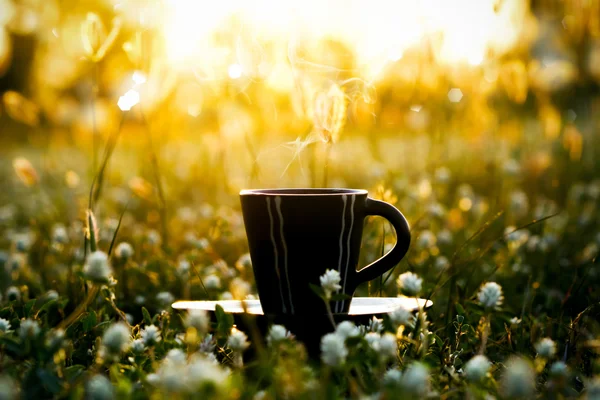 Caffè del mattino con tazza nera sullo sfondo erba fiore . — Foto Stock