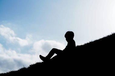 Tepede oturan siluet çocuk gökyüzü arka planıyla.