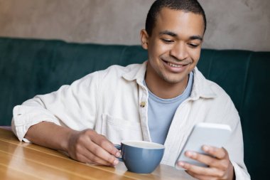 Gülümseyen ve kahve dükkanında akıllı telefondan mesajlaşan Afrikalı genç bir Amerikalı. 