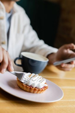 Afro-Amerikan bir adamın lezzetli tart ve kapuçino bardağının yanında çatal tutarken çekilmiş görüntüsü. 
