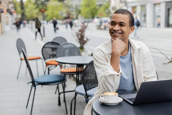 Tersenyum African American Freelancer Berpaling Dekat Laptop Dan Secangkir Cappuccino — Stok Foto