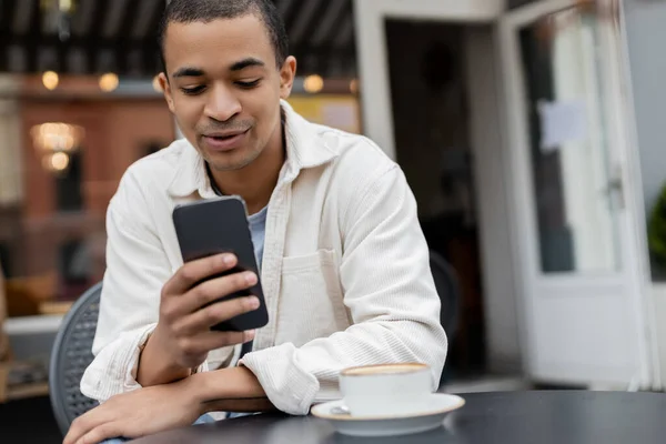 Hombre Afroamericano Mensajes Texto Teléfono Inteligente Cerca Taza Capuchino Mesa — Foto de Stock