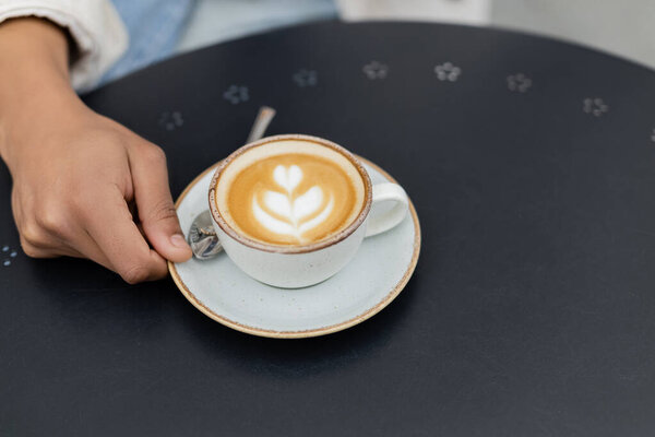 высокий угол зрения африканский американец держит блюдце с чашкой капучино на летней террасе 