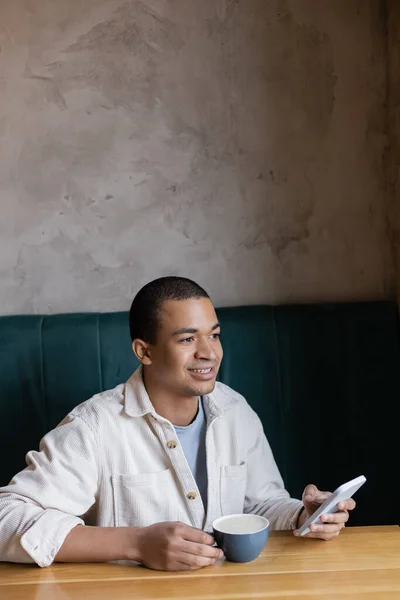 Usmívající Mladý Africký Američan Drží Smartphone Drží Cappuccino Kavárně — Stock fotografie