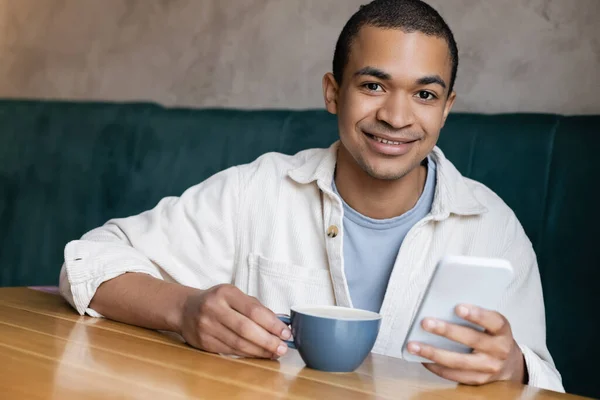 Pozitivní Mladý Africký Americký Muž Zprávy Smartphone Kavárně — Stock fotografie