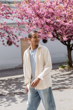 Pozitif Afro-Amerikan gömlekli adam Pembe kiraz ağacının yanında yürüyor