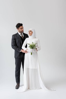 Müslüman damat, gri buketli gelinlik içinde neşeli geline sarılıyor. 