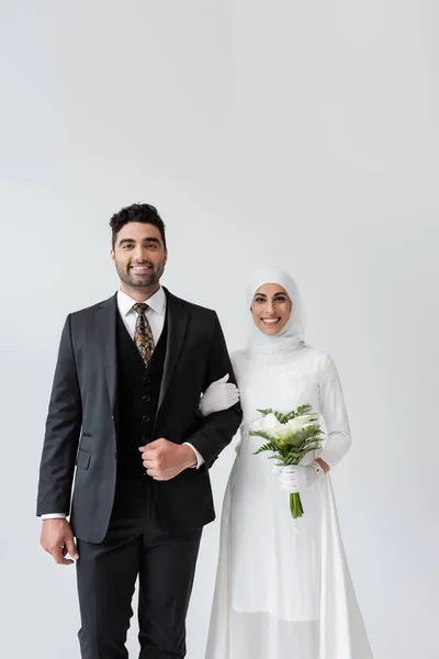 Šťastná Muslimská Nevěsta Kyticí Stojící Poblíž Veselého Ženicha Izolované Šedé — Stock fotografie
