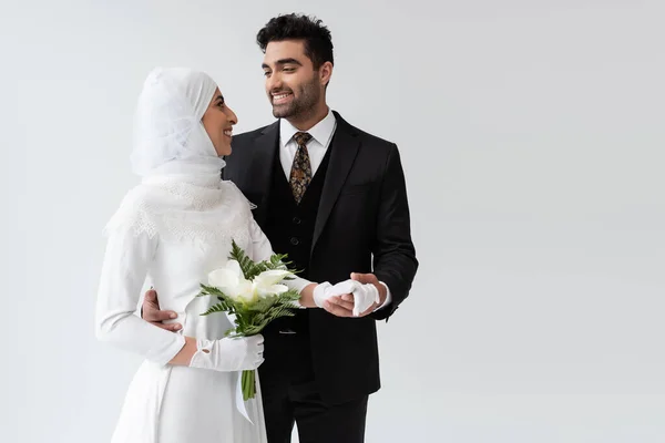 穆斯林新郎牵着笑容满面的新娘的手 身穿婚纱 花束与灰色隔离 — 图库照片