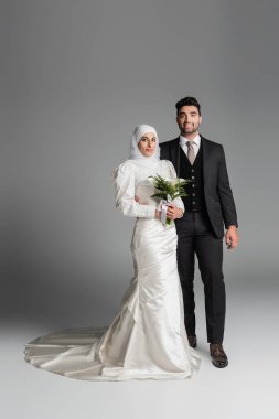 Takım elbiseli mutlu bir damat. Gri buketli Müslüman gelinin yanında.