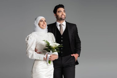 Takım elbiseli damat, gri buketli mutlu gelinin yanında poz veriyor.