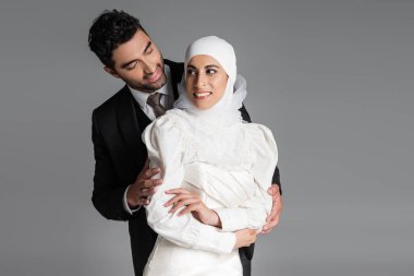 Gülümseyen damat, gri gelinlik içinde neşeli gelinin arkasında dikiliyor.