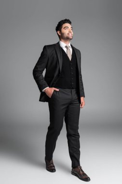 Takım elbiseli şık Müslüman damadın gri üzerinde dururken el ele poz verişi.