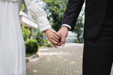cropped view of bride in wedding ring holding hands with groom outdoors  clipart
