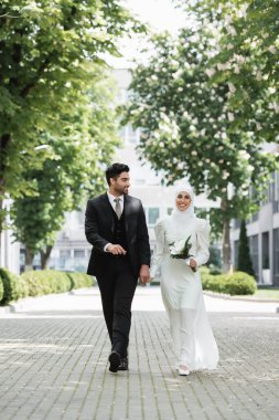 Mutlu damat, Müslüman gelinle el ele tutuşuyor düğün buketi ile ve birlikte yürüyor. 