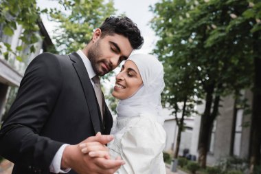 Neşeli Müslüman yeni evliler. Gözleri kapalı, el ele tutuşuyorlar.