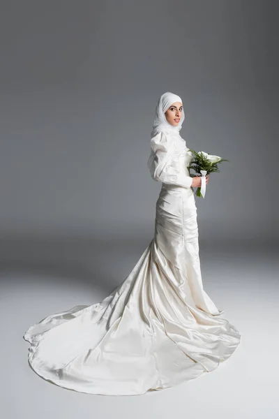 イスラム教徒の花嫁の完全な長さのビューで豪華な結婚式のドレスは灰色の花束で立って — ストック写真