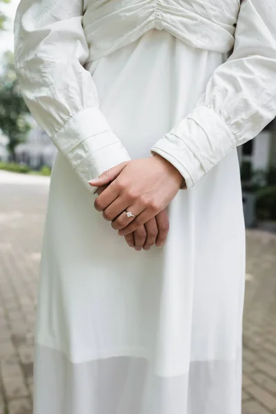 cropped view of bride in wedding dress with diamond ring on finger standing outside