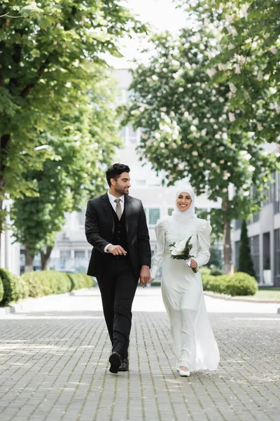 Счастливый Жених Держась Руки Мусульманской Невестой Свадебным Букетом Гуляя Вместе — стоковое фото